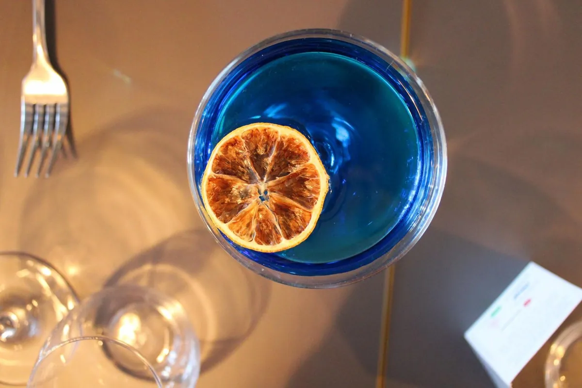 A blue cocktail with a dried orange slice, seen from above on a table
