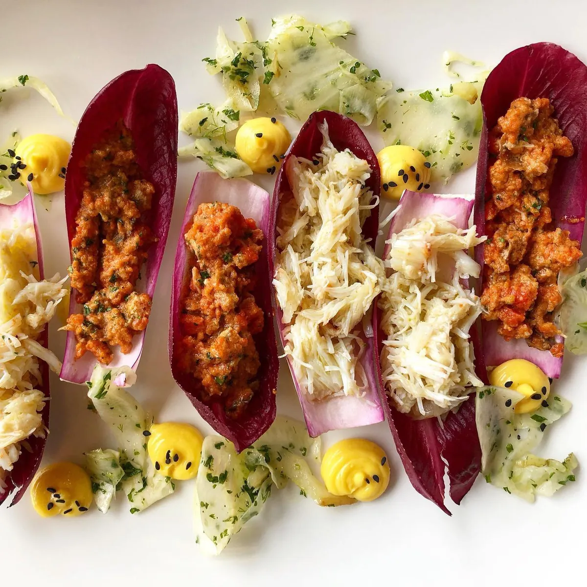 White crab meat and a red, chunky crab mixture served in red chicory leaves, with shaved fennel and dots of yellow mayonnaise