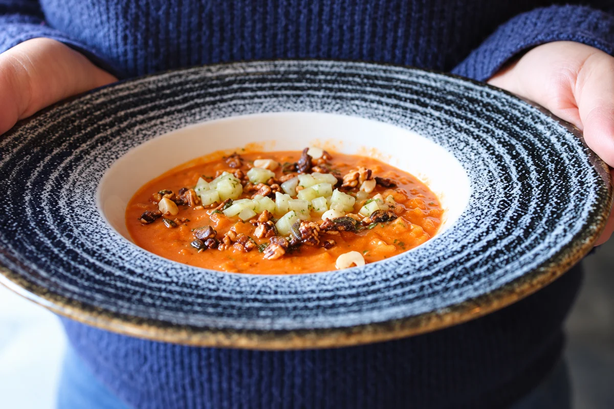 Two hands holding a textured ceramic bowl containing an orange dish with garnish