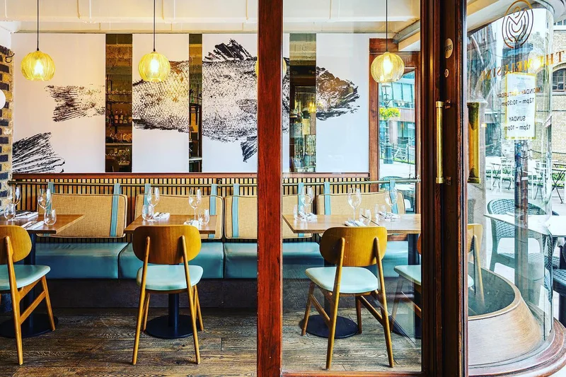 The dining room with fish artwork, teal seating and tables set for guests