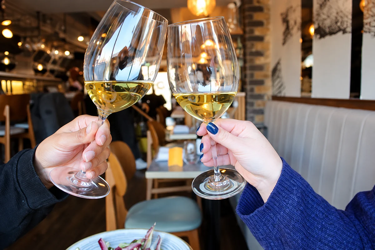 Two guests raising glasses of white wine in a toast inside The Melusine