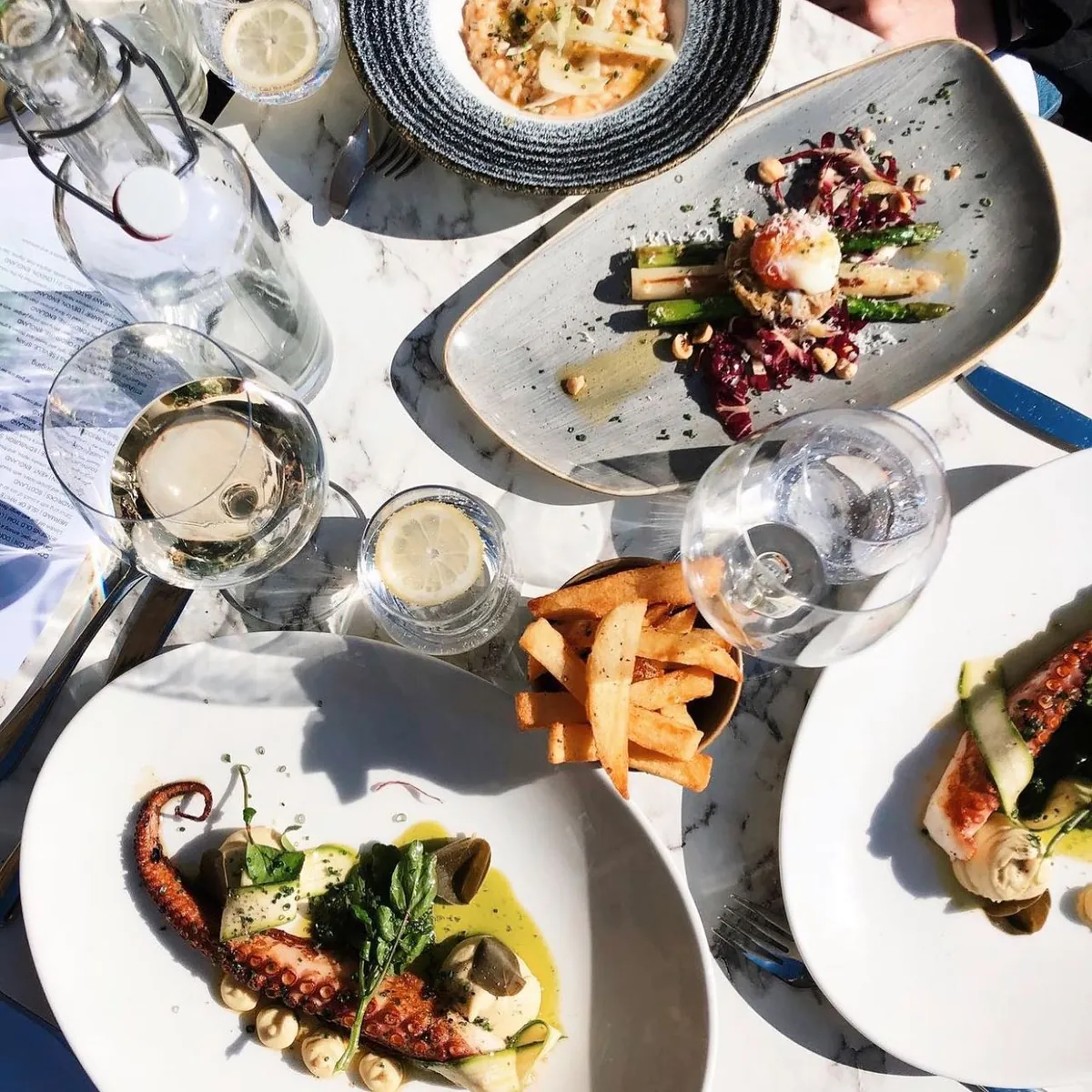 Seafood dishes and chips on a table with glasses of white wine