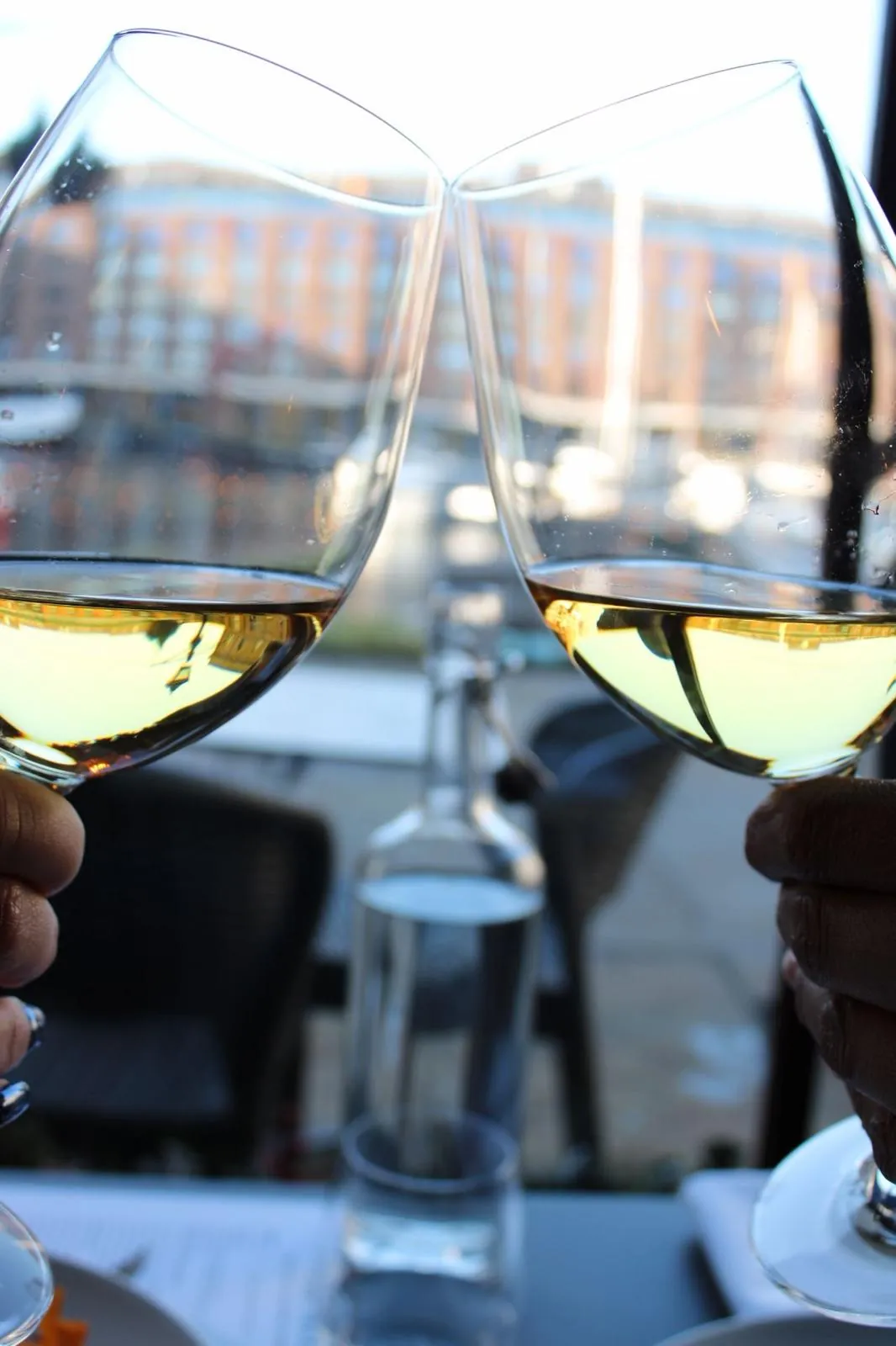Two glasses of white wine raised in a toast, with the docks in the background